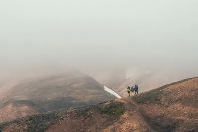 Zwei Wanderer mit Rucksäcken auf einem Grat, fast verschluckt von dichtem Nebel