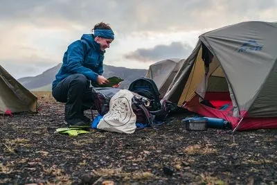 Eine Wanderin in blauer Jacke sortiert neben ihrem Zelt auf einem Zeltplatz im Hochland ihre Ausrüstung
