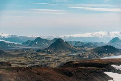 Blick über das Hochland mit Schneefeldern, dunklen Gipfeln und einem Gletscher in der Ferne, aufgenommen auf dem Laugavegur Ende Juli 2026